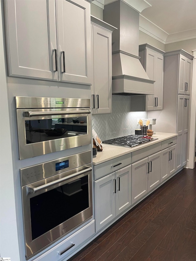 kitchen featuring appliances with stainless steel finishes, premium range hood, ornamental molding, dark hardwood / wood-style flooring, and decorative backsplash