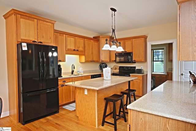 kitchen with black appliances, sink, a kitchen island, a breakfast bar, and light hardwood / wood-style flooring