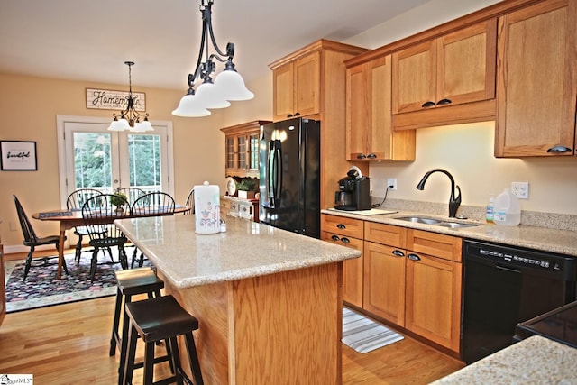 kitchen featuring light hardwood / wood-style flooring, a center island, light stone counters, black appliances, and sink