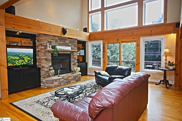 living room with a stone fireplace, a towering ceiling, built in shelves, and light hardwood / wood-style flooring