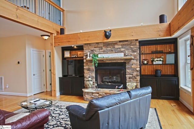 living room featuring built in features, a high ceiling, a fireplace, and light hardwood / wood-style flooring