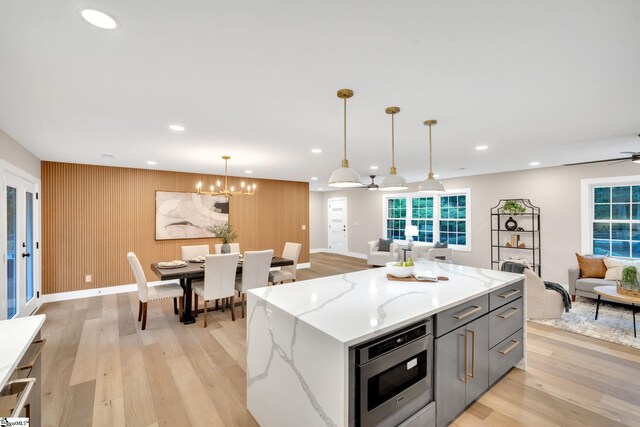 kitchen featuring wall oven, ceiling fan with notable chandelier, pendant lighting, light wood-type flooring, and light stone countertops