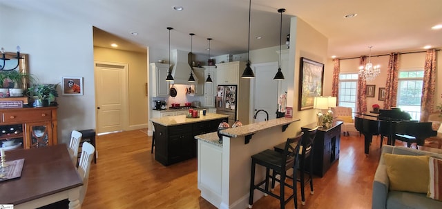 kitchen featuring decorative light fixtures, light wood-type flooring, island exhaust hood, a kitchen island, and a breakfast bar