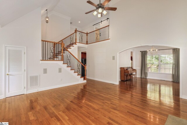 unfurnished living room with high vaulted ceiling, ceiling fan with notable chandelier, and hardwood / wood-style floors