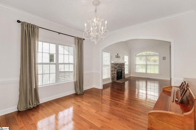 living room with a stone fireplace, wood-type flooring, a notable chandelier, and ornamental molding