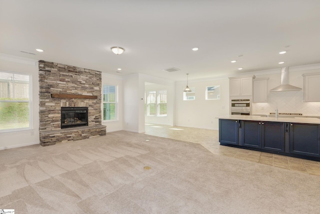 unfurnished living room featuring a stone fireplace, ornamental molding, and light colored carpet