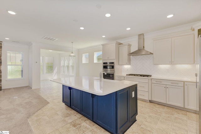 kitchen featuring white cabinets, an island with sink, wall chimney exhaust hood, light colored carpet, and backsplash