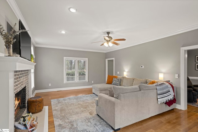 living room featuring wood-type flooring, a brick fireplace, ceiling fan, and crown molding