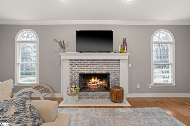 living room with wood-type flooring, a brick fireplace, and ornamental molding