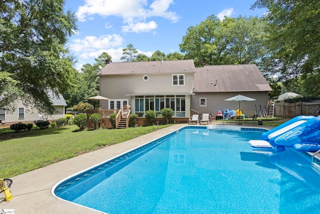 view of pool featuring a wooden deck, a sunroom, a water slide, and a lawn