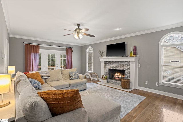 living room featuring a brick fireplace, crown molding, wood-type flooring, and ceiling fan