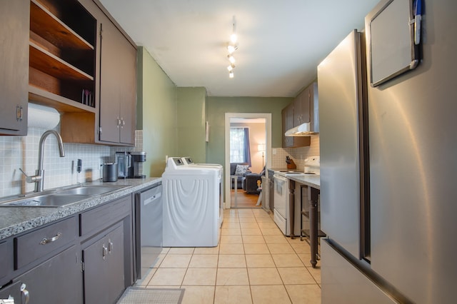 kitchen with sink, washer and dryer, light tile patterned floors, appliances with stainless steel finishes, and decorative backsplash