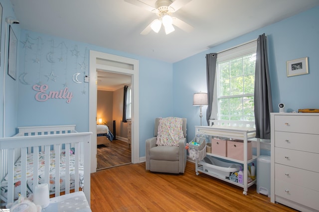 bedroom with a nursery area, ceiling fan, and light hardwood / wood-style floors