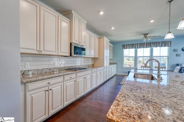 kitchen with dark wood-type flooring, ceiling fan, stainless steel appliances, light stone countertops, and sink