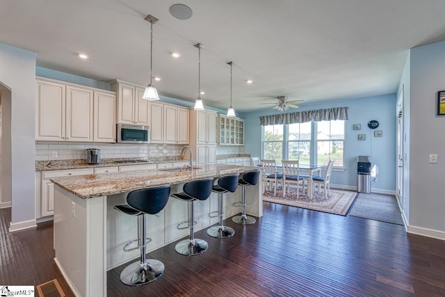 kitchen with dark wood-type flooring, backsplash, stainless steel appliances, hanging light fixtures, and a large island with sink