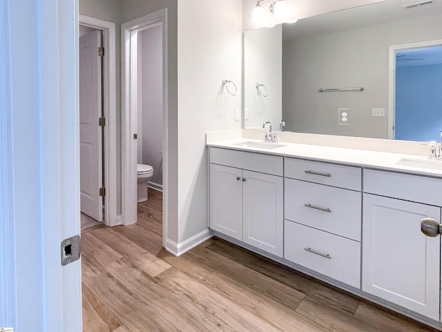 full bath featuring double vanity, toilet, wood finished floors, and a sink