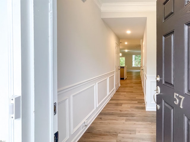 corridor featuring crown molding, light wood-style flooring, a decorative wall, and a wainscoted wall