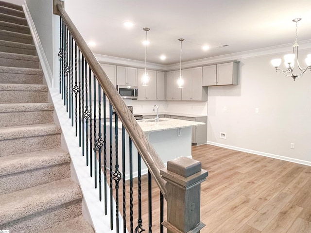 stairs featuring wood-type flooring, an inviting chandelier, crown molding, and sink