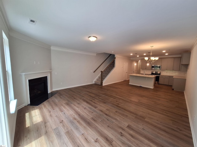 unfurnished living room featuring an inviting chandelier, sink, crown molding, and hardwood / wood-style flooring