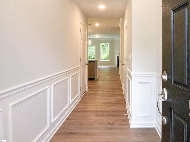 hallway with recessed lighting, a wainscoted wall, light wood-style floors, and a decorative wall