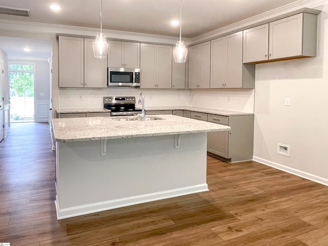 kitchen featuring a kitchen island with sink, dark wood-type flooring, appliances with stainless steel finishes, crown molding, and light stone countertops