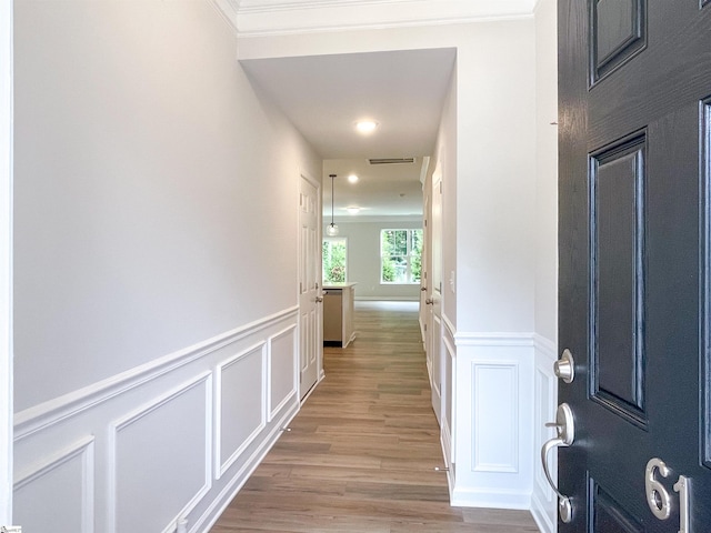 hall featuring visible vents, a decorative wall, a wainscoted wall, and light wood finished floors