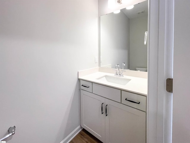 bathroom featuring visible vents, baseboards, toilet, wood finished floors, and vanity