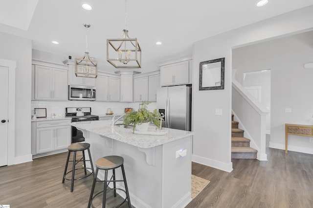 kitchen with a kitchen island with sink, recessed lighting, stainless steel appliances, wood finished floors, and a kitchen breakfast bar