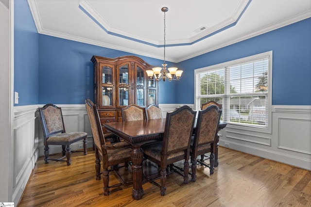 dining space with hardwood / wood-style flooring, a notable chandelier, ornamental molding, and a tray ceiling