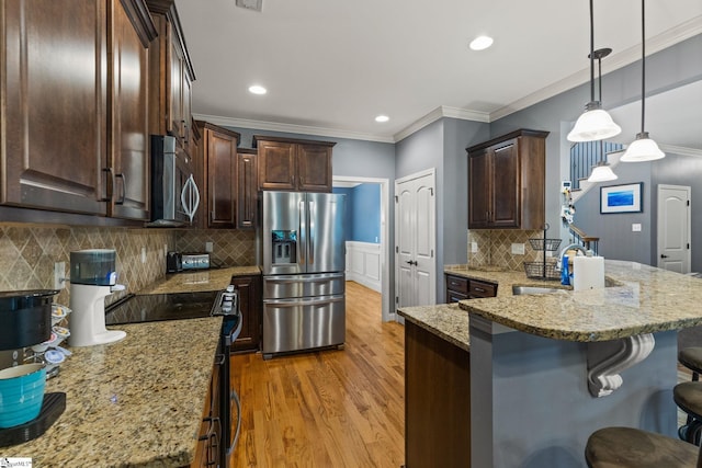 kitchen featuring light hardwood / wood-style floors, appliances with stainless steel finishes, decorative backsplash, dark brown cabinetry, and a kitchen bar