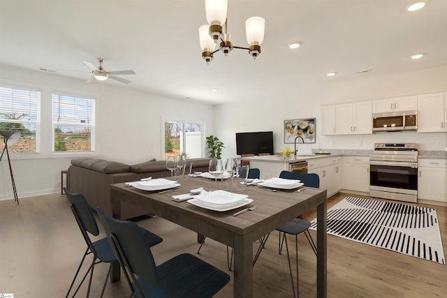 dining space with light wood finished floors, recessed lighting, ceiling fan with notable chandelier, and baseboards