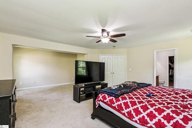 carpeted bedroom with ceiling fan, a closet, ensuite bath, and baseboards