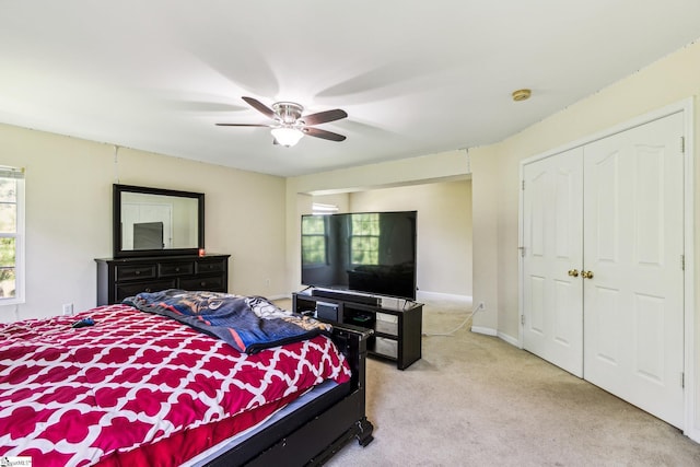 bedroom with a closet, light carpet, ceiling fan, and baseboards