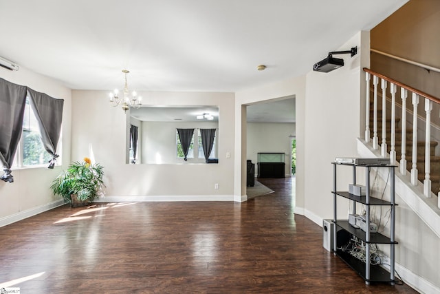 spare room with a healthy amount of sunlight, stairway, an inviting chandelier, and wood finished floors