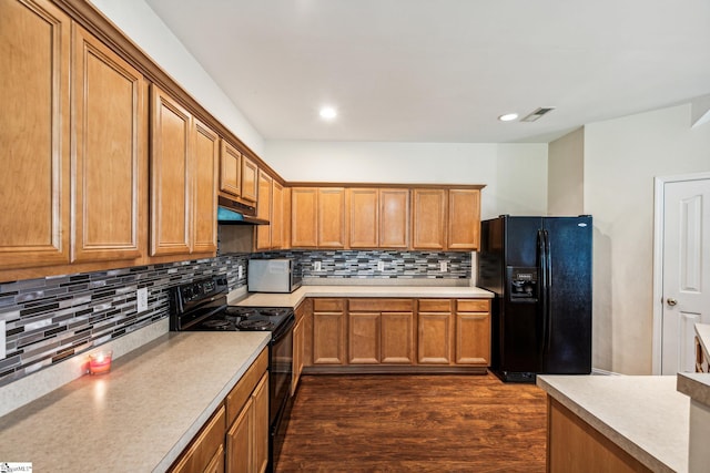 kitchen with brown cabinetry, visible vents, under cabinet range hood, and black appliances