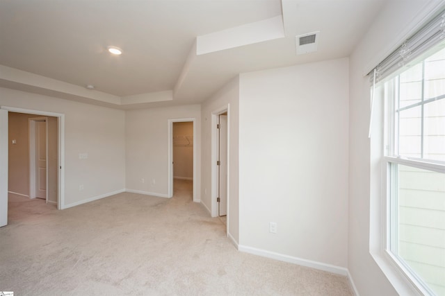 empty room featuring a tray ceiling, light carpet, and a healthy amount of sunlight