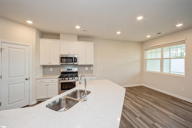 kitchen with appliances with stainless steel finishes, hardwood / wood-style flooring, light stone counters, and white cabinetry