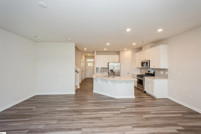 kitchen featuring tasteful backsplash, stainless steel appliances, white cabinetry, and a center island with sink