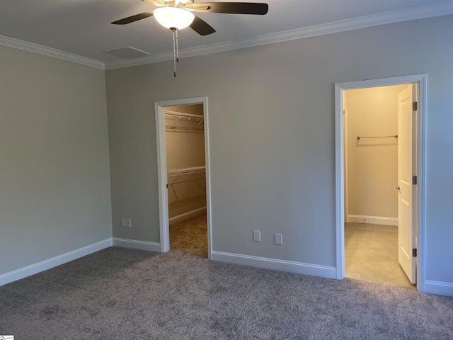 unfurnished bedroom with a closet, a spacious closet, carpet floors, baseboards, and ornamental molding