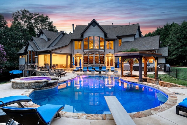 pool at dusk featuring a patio, a diving board, and an in ground hot tub