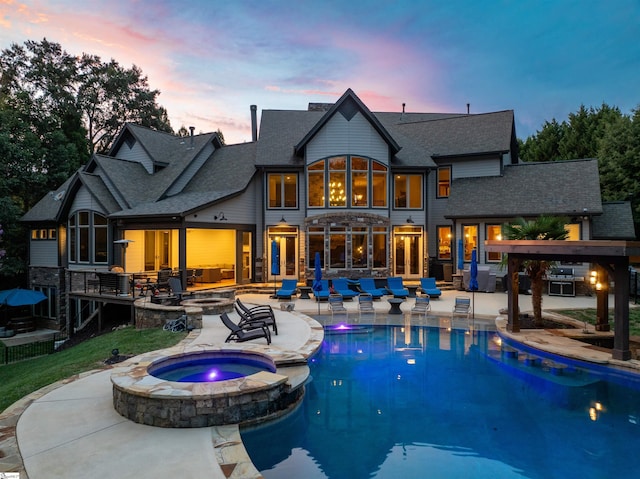 back house at dusk featuring a swimming pool with hot tub and a patio area