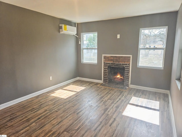 unfurnished living room with a wall mounted AC, a fireplace, wood finished floors, and baseboards