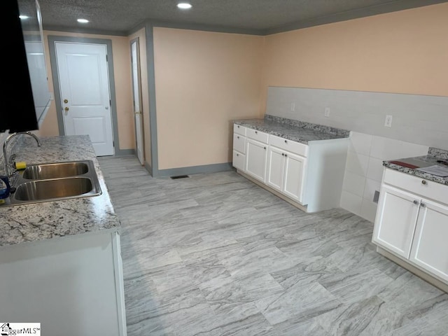 kitchen featuring white cabinetry, sink, light stone countertops, a textured ceiling, and light tile patterned floors