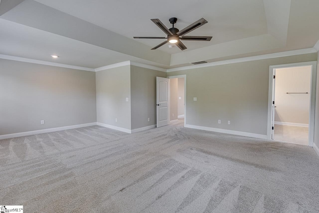 unfurnished room with a tray ceiling, crown molding, light colored carpet, visible vents, and baseboards