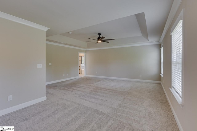 unfurnished room featuring light colored carpet, a ceiling fan, baseboards, a tray ceiling, and crown molding