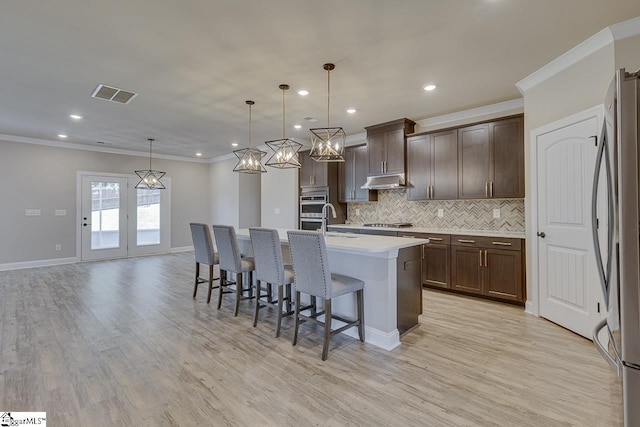 kitchen featuring pendant lighting, light countertops, visible vents, appliances with stainless steel finishes, and an island with sink