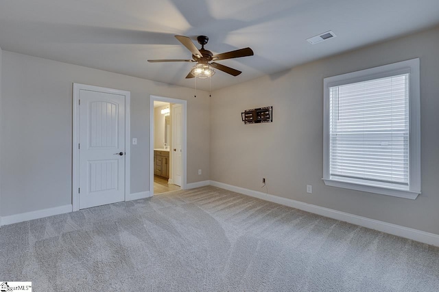 unfurnished bedroom with light colored carpet, visible vents, a ceiling fan, ensuite bath, and baseboards