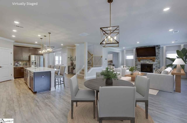 dining space with ornamental molding, a stone fireplace, light wood finished floors, and stairs