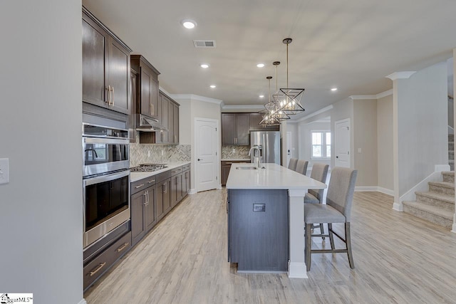 kitchen with decorative light fixtures, light countertops, appliances with stainless steel finishes, an island with sink, and a kitchen bar