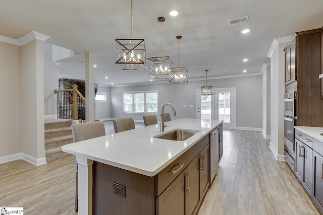 kitchen featuring light countertops, hanging light fixtures, open floor plan, a kitchen island with sink, and a sink